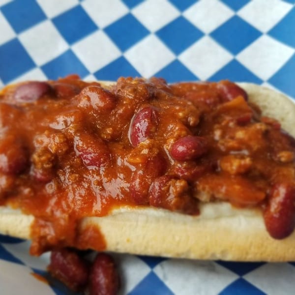 A chili dog from Big Ray's Burgers & Dogs, topped with hearty chili and beans, on blue and white checkered paper.